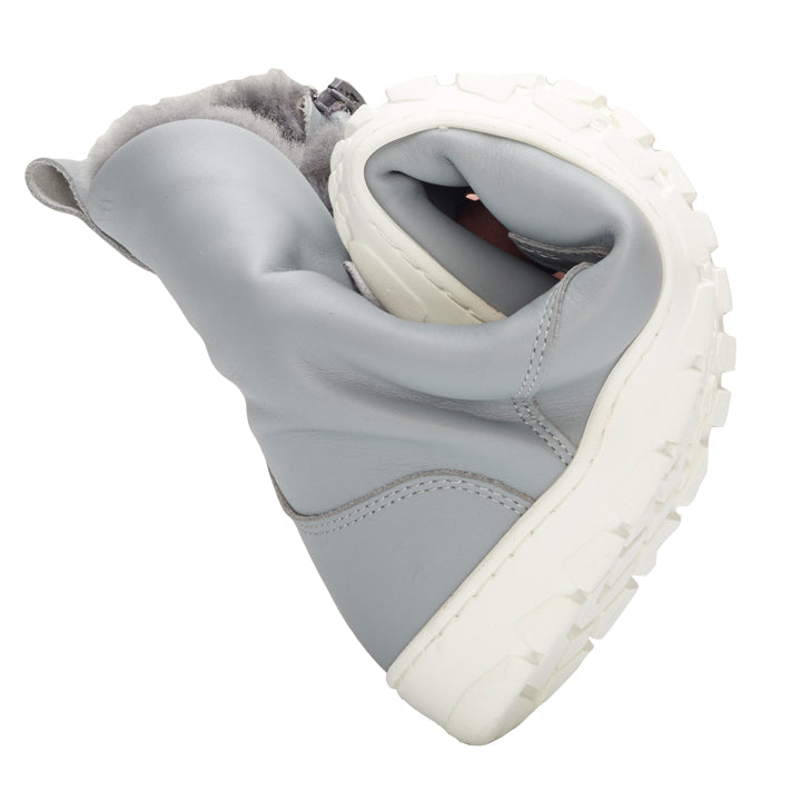 A QUINTIC Winter Blue Grey a ZAQQ-tól egy rugalmas téli csizma szürke színben, vastag fehér talppal, amely középen hajlik, hogy kiemelje hajlékonyságát. A csizma puha nappabőrből készült, belül pedig puha, bolyhos béléssel van ellátva.