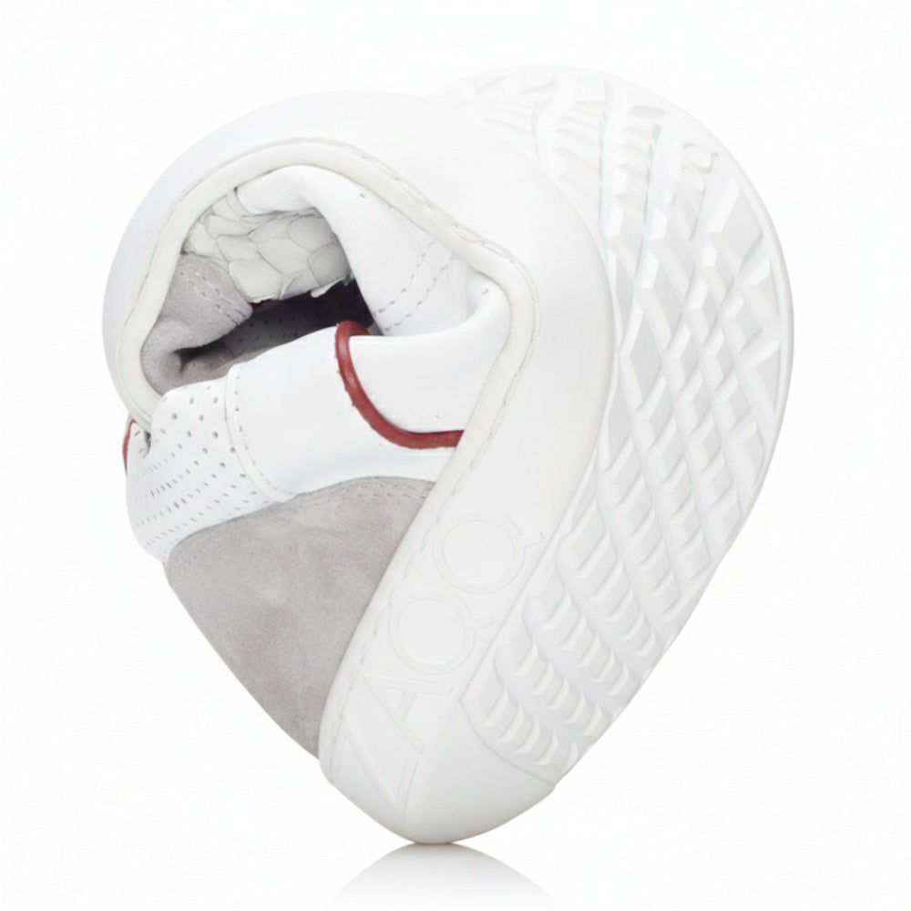Der weiße Sneaker QLERQ von ZAQQ zeichnet sich durch graue und rote Akzente aus, die zu einem Herz geformt sind. Er ist aus Veloursleder gefertigt und seine Sohle weist ein detailliertes Profilmuster auf, das die Marke ZAQQ repräsentiert. Dieser modische Barfußschuh verbindet nahtlos Komfort mit unverwechselbaren Designelementen.