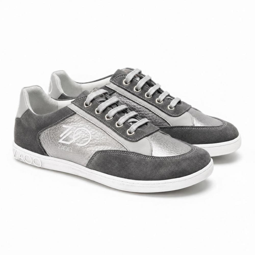 Egy pár OQTAV Grey-sneaker a ZAQQ-tól, bársonyos velúrból és strukturált betétekkel készült. Ezüst fűzőkkel és az oldalán és sarkán található jellegzetes Zagoo-logóval ezek a stílusos cipők egymás mellett egy fehér háttéren kerülnek bemutatásra.