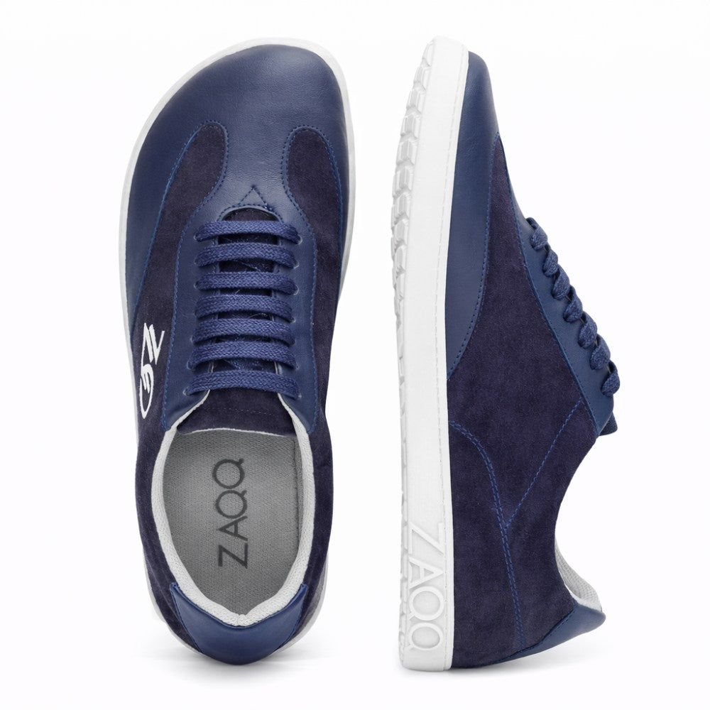 Egy pár Queensburry Marine sneaker sötétkék bőrből kiállítva, az egyik cipő állva, a másik oldalra fektetve. Ezek a cipők vadbőr és bőr textúrák kombinációjával, gumitalppal és cipőfűzőkkel rendelkeznek, hogy maximális kényelmet nyújtsanak járás közben. A ZAQQ márkanév látható a talpbetéten és a talp oldalán.