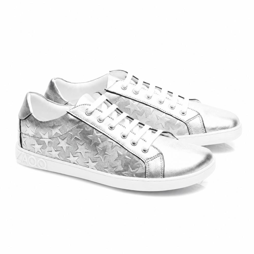 A ZAQQ SLOQ Stars Silver-Sneaker fehér cipőfűzővel és csillagmintával rendelkezik az oldalán, kiegészítve egy fehér talppal, amelynek sarkán VAOO dombornyomás található. Ezeket a cipőket karcsú és modern dizájn jellemzi, fényes metálfényezéssel.
