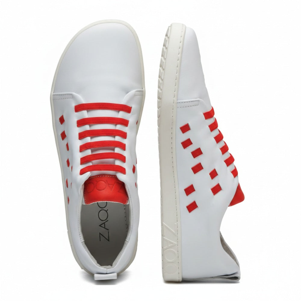 STRAQ Weiße Sneaker von ZAQQ mit roten Gummibändern und seitlichen Aussparungen. Ein Schuh steht aufrecht, während der andere auf der Seite liegt und eine transparente Sohle mit dem Aufdruck „Zaoq“ zeigt. Diese Sneaker sind in einem modernen, minimalistischen Design aus hochwertigem Nappaleder gefertigt und verleihen dadurch noch mehr Eleganz.