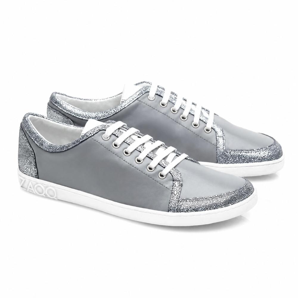 A TIQQ Grey Silver Sneaker a ZAQQ-tól lenyűgöz egyszerű dizájnjával, amely puha nappabőrből készült, fehér cipőfűzőkkel és ezüst csillogó akcentusokkal, kiegészítve fehér talpakkal és egy diszkrét logóval a saroknál, és tökéletes keveréket kínál stílusból és kényelemből minden alkalomra.